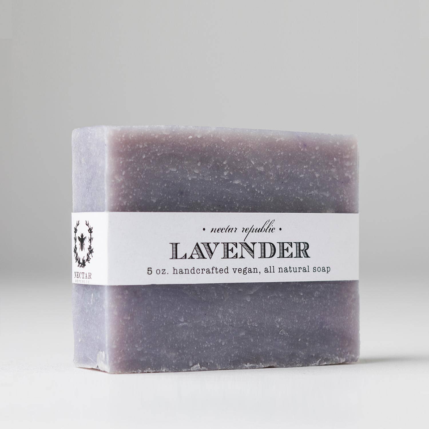 A bar of "Lavender : Bath Soap" features a white label showcasing "Nectar Republic" and "5 oz. handcrafted vegan, all natural soap," enriched with calming lavender essential oil for a peaceful experience.