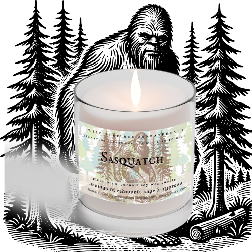 A lit Candle - Tropical Rain by Heaven & Earth Aromatherapy sits before a black and white Sasquatch pine forest illustration. The label highlights refreshing tropical aromatics for an immersive, nature-inspired vibe.