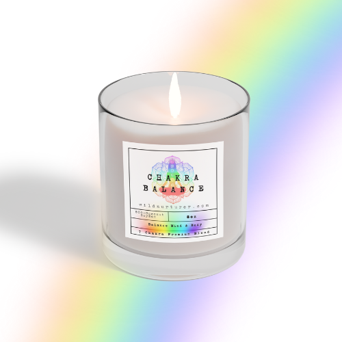 The lit Chakra Candle - Coconut Soy Wax Candle 8oz by Heaven & Earth Aromatherapy glows in a clear glass jar with "Chakra Balance" label, casting a rainbow reflection—ideal for meditation.