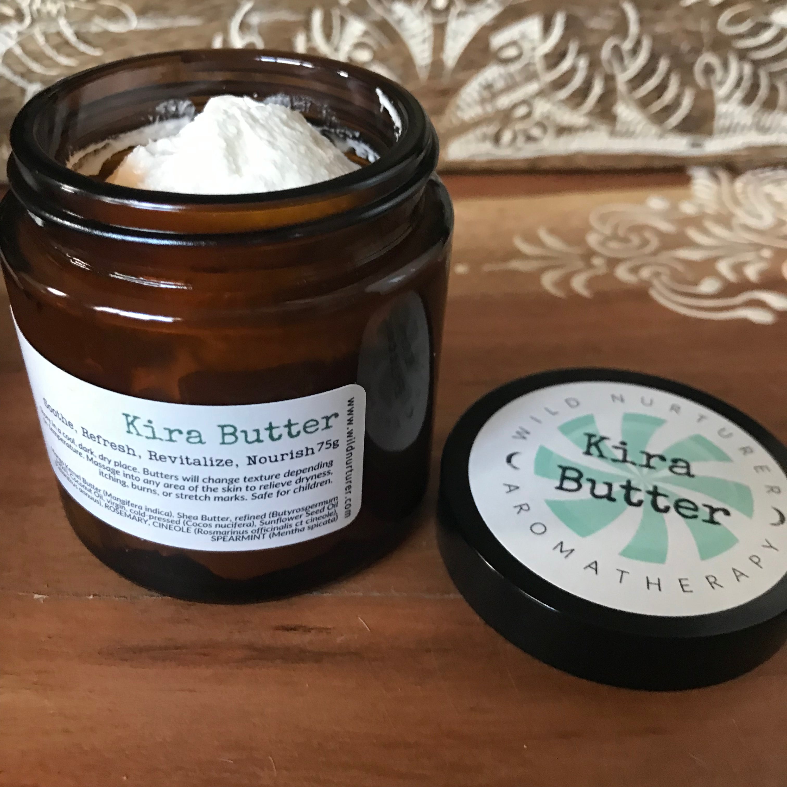 A glass jar of Wild Nurturer Aromatherapy Kira's Collection Rosemary & Mint Body Butter with a white label against a white background. The label includes product details and a green leaf design.