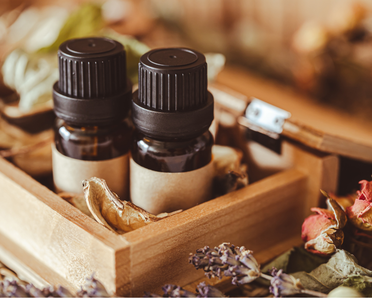 Two small essential oil bottles in a wooden box surrounded by dried flowers and herbs.