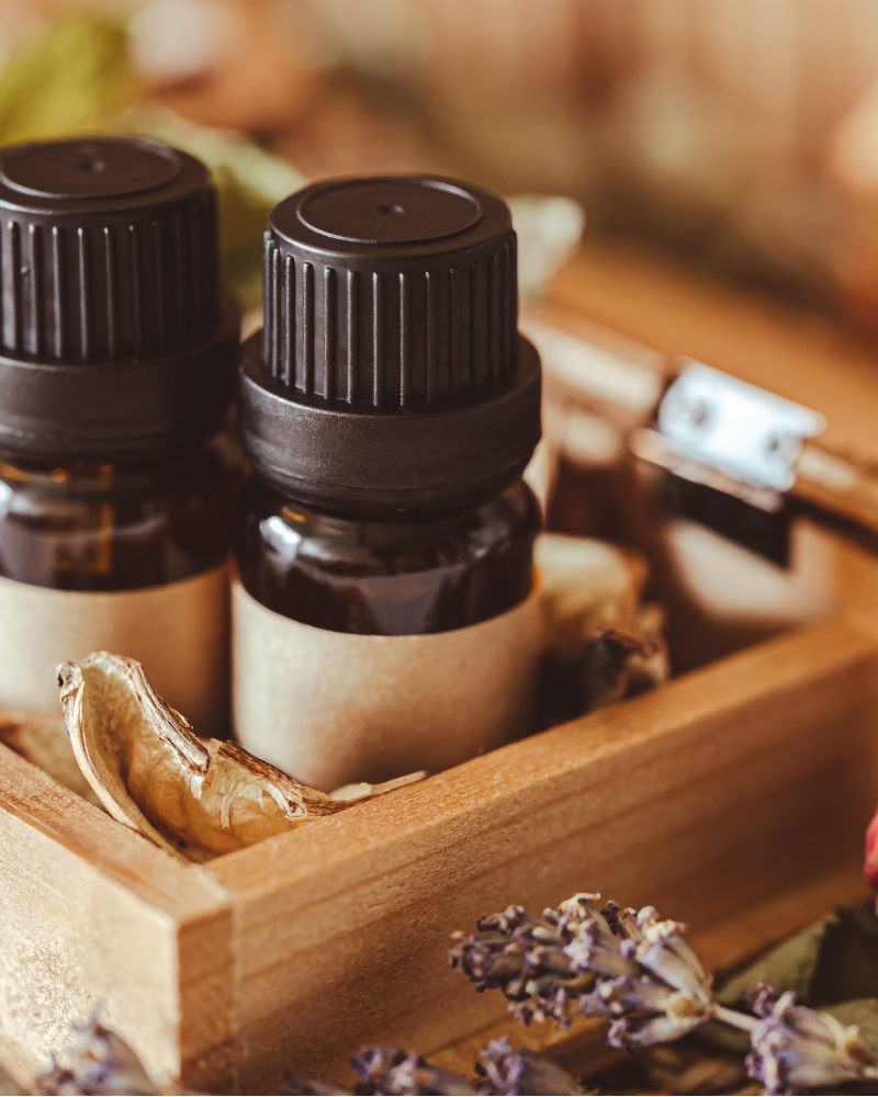 Two small essential oil bottles in a wooden box surrounded by dried flowers and herbs.
