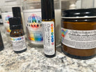 A selection of Wild Nurturer Aromatherapy’s Chakra Balance Aromatherapy - 7 Aromatic Essences (Bulk Pack of 6), including a small essential oil bottle, a roller, a jar, and a candle for aromatherapy and chakra balancing, displayed on a speckled countertop.