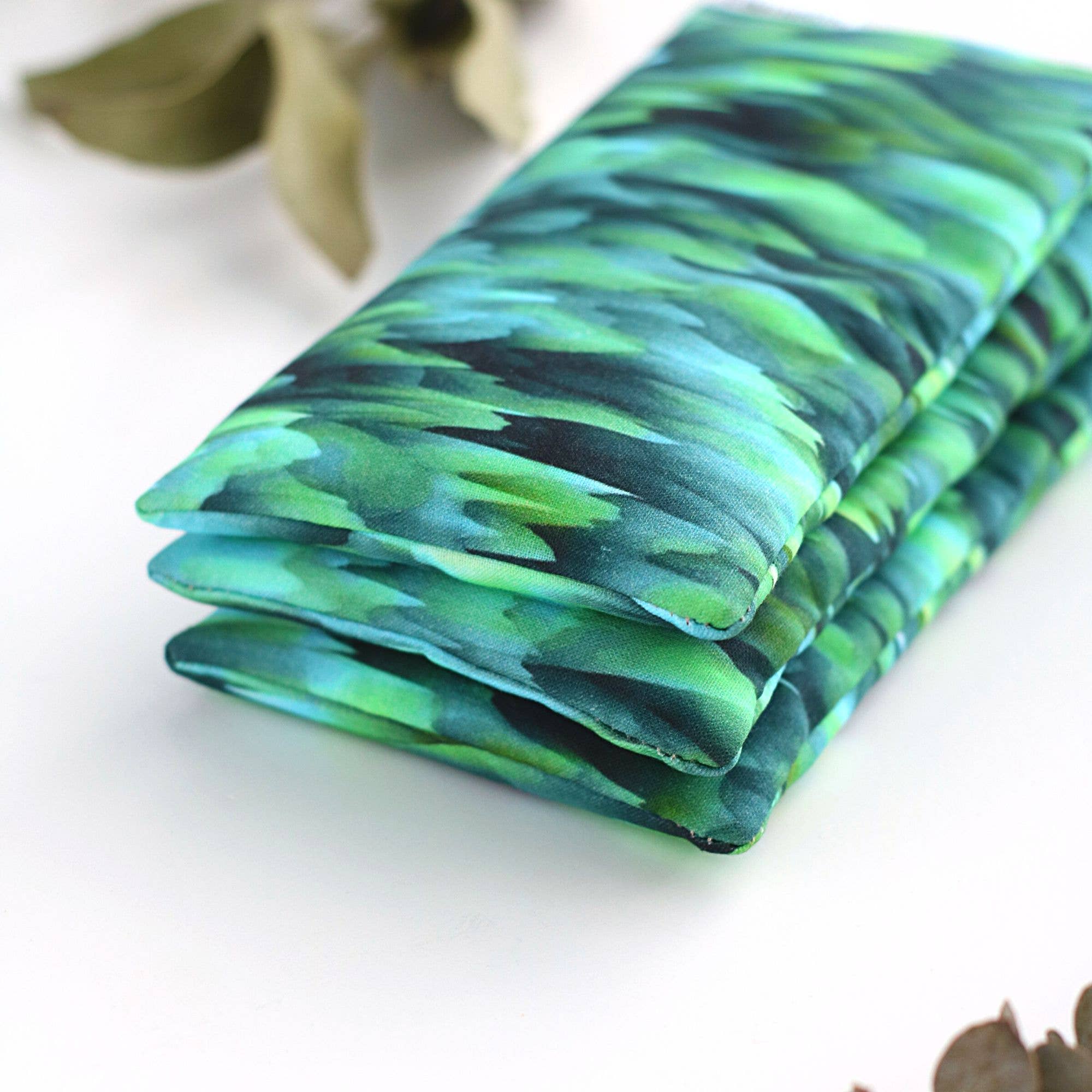 Three Breathe Gift Sets: Winter Eucalyptus Eye Pillows & Handmade Breathe Balms with green and blue tie-dye patterns, displayed on a white background surrounded by eucalyptus leaves from SaidoniaEco.