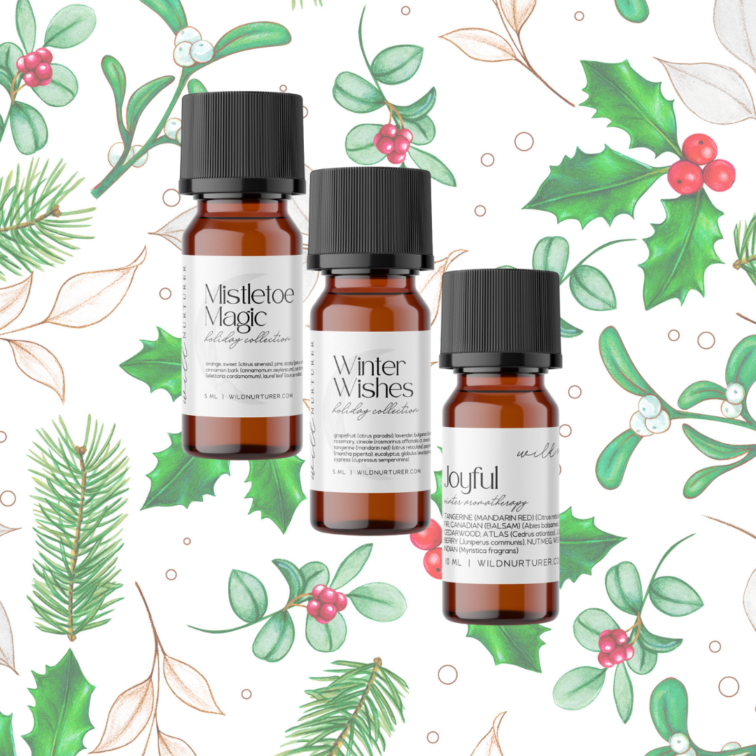 Three essential oil bottles labeled "Deck the Halls Holiday Aromas Diffuser Gift Set," "Winter Spice," and "Evergreens" from Heaven & Earth Aromatherapy, surrounded by illustrated mistletoe and pine.