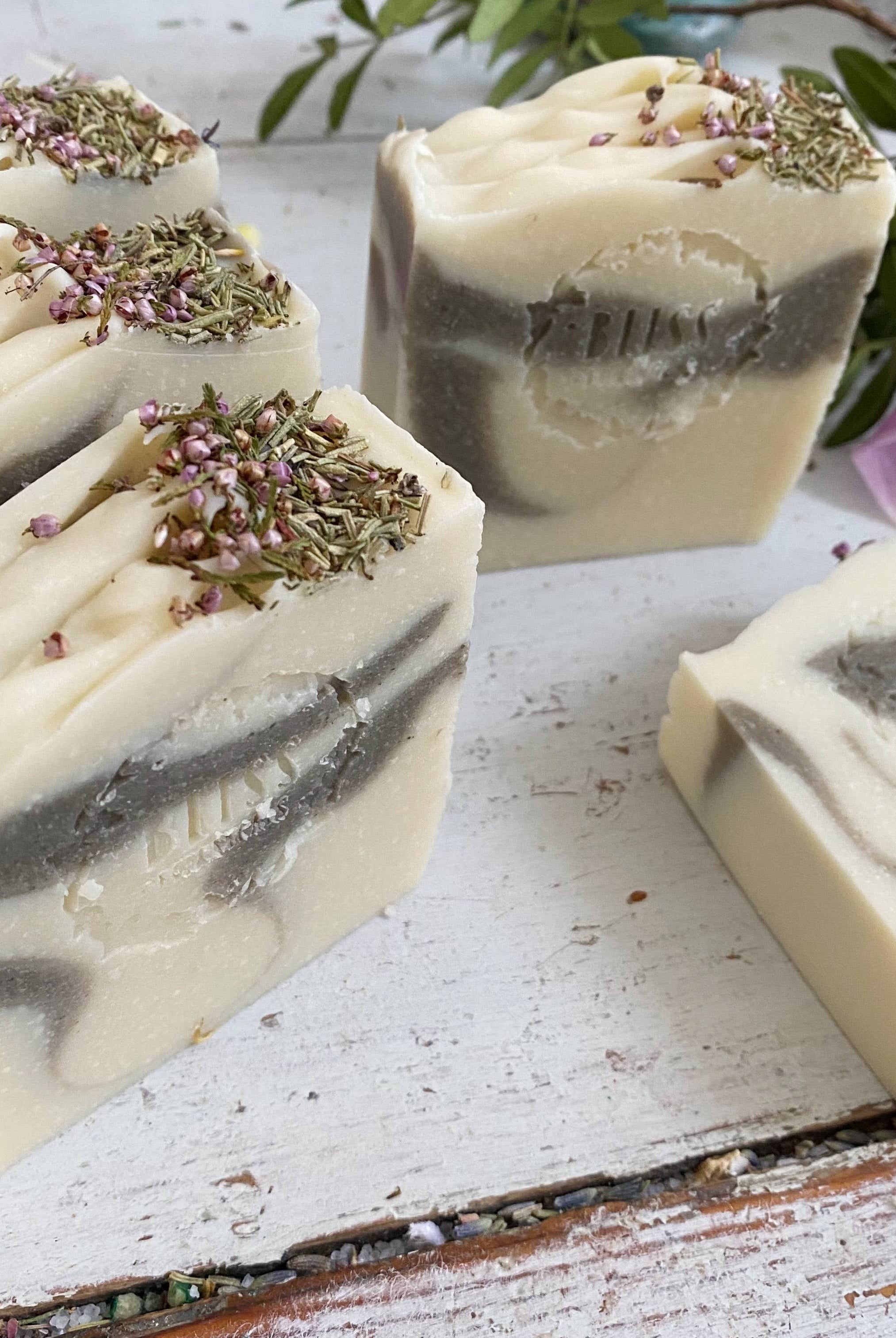 Bliss Botanicals Forest Fairy Soap bars with lavender buds and aromatherapy essential oil displayed alongside pink petals and green leaves, featuring a label titled "forest fairy" on a rustic white background.