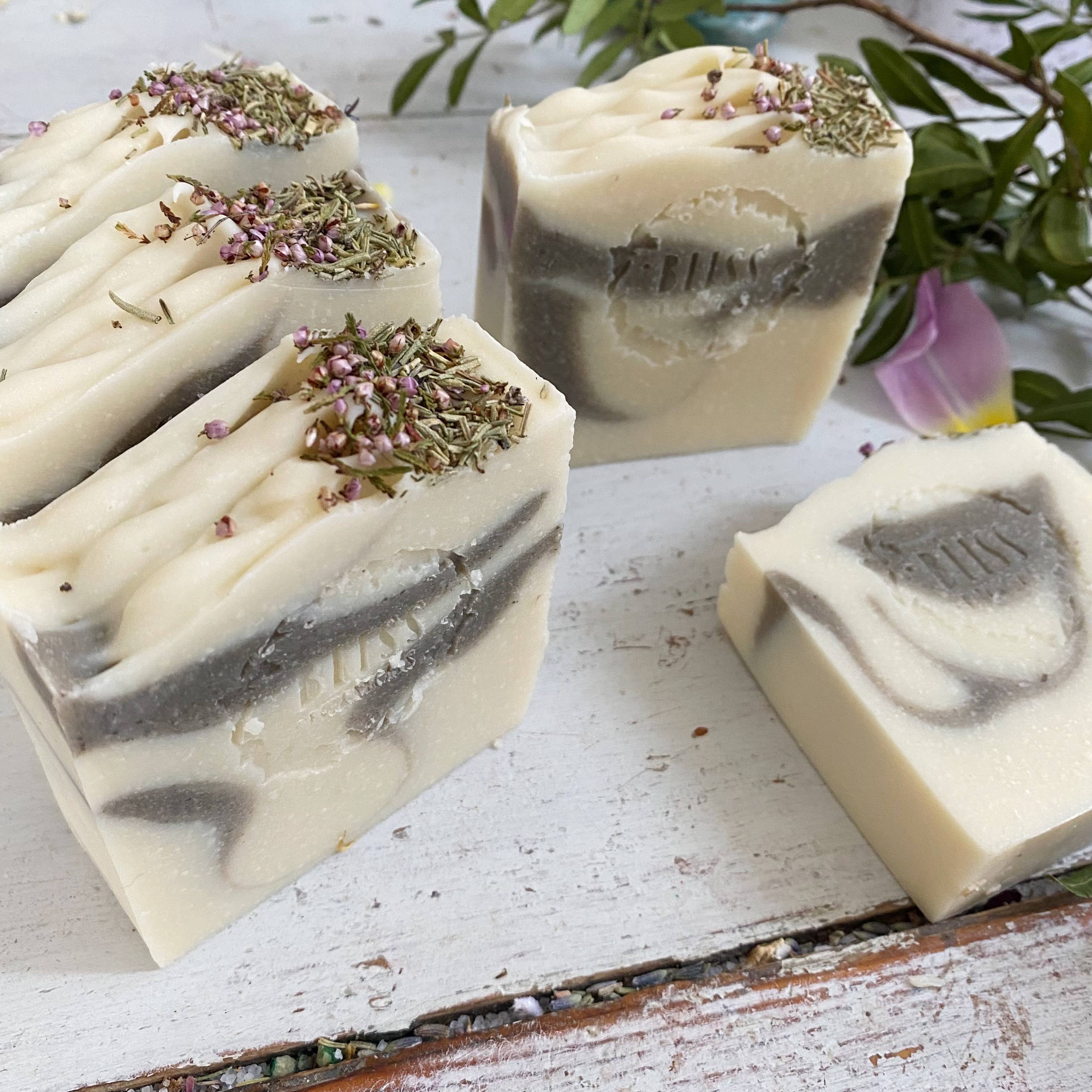 Bliss Botanicals Forest Fairy Soap bars with lavender buds and aromatherapy essential oil displayed alongside pink petals and green leaves, featuring a label titled "forest fairy" on a rustic white background.