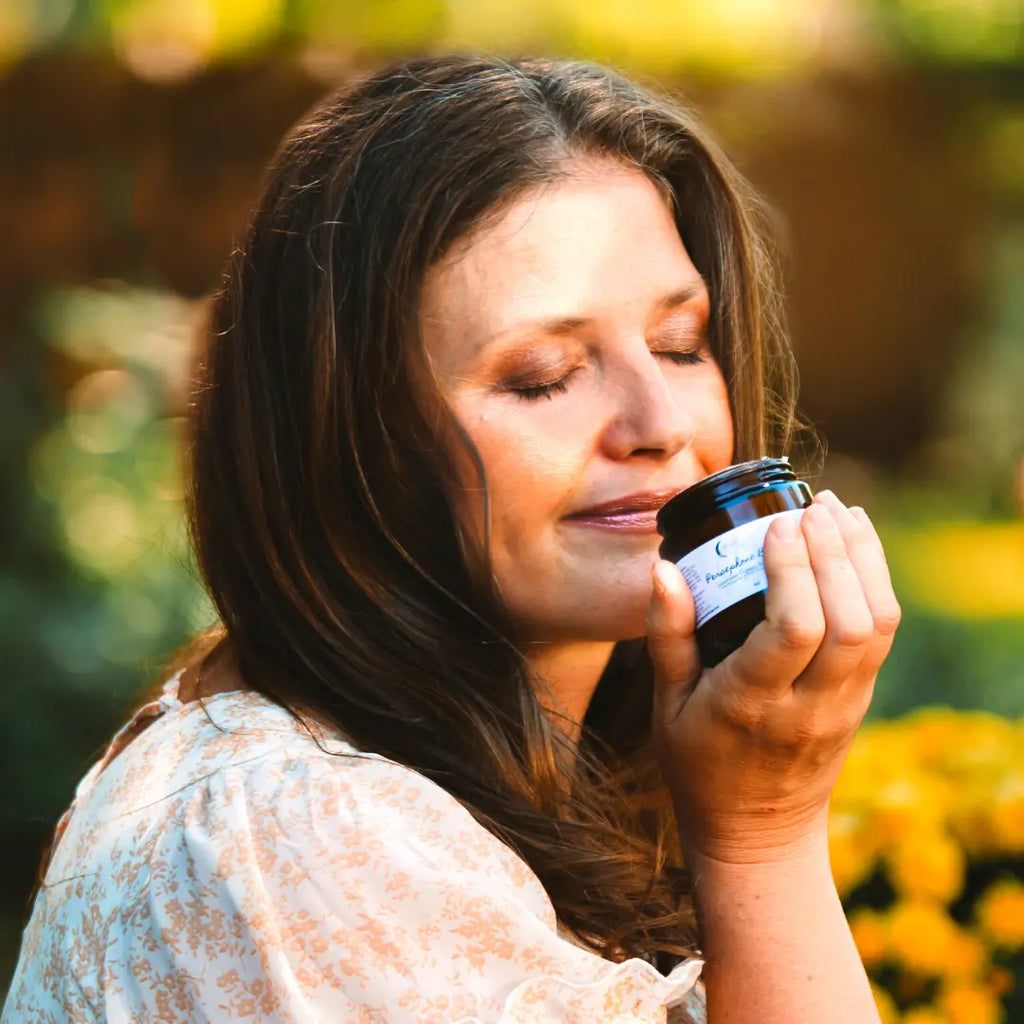 Woman with eyes closed, smiling, smelling a jar of body butter