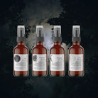 Five bottles of Moon Medicine Collection essential oil skincare products with spray nozzles, labeled with moon phases, against a dark, misty forest background.