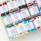 Open box containing various sets of colorful fabric bags labeled "for kids," showcasing different patterns and designs, scented with wild nurturer aromatherapy featuring SaidoniaEco Boo Boo Healing Kit For Kids - Features Hot Cold Rice Pack with Mama Gaia Salve.