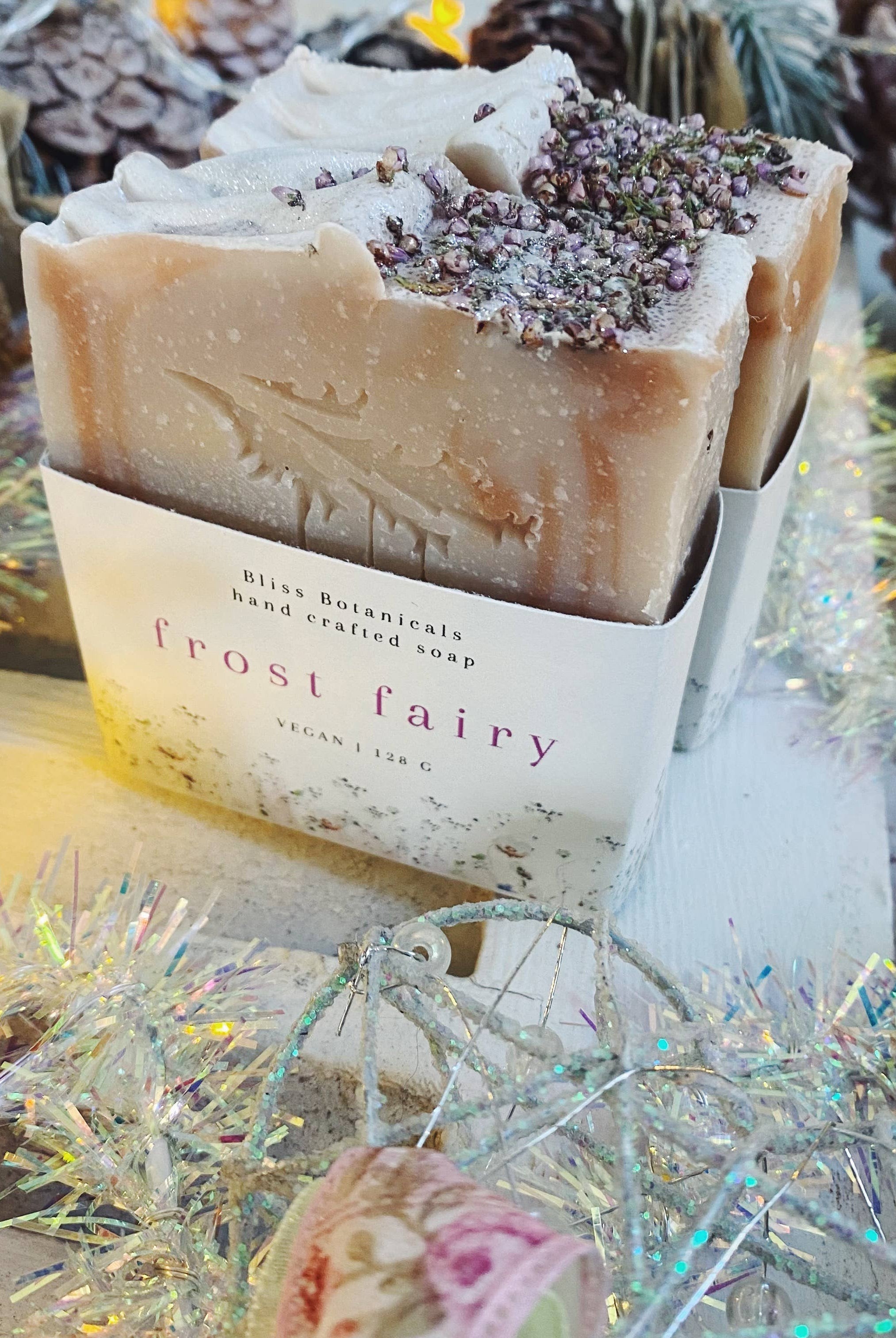 Handmade Bliss Botanicals Frost Fairy Soap displayed with pine cones and fairy lights on a rustic wooden surface.