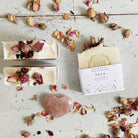 Handmade Love Soap - Rose Geranium with Rose buds soap bars, featuring a heart-shaped pink stone, on a rustic white wooden surface by Bliss Botanicals.