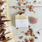 Handmade Love Soap - Rose Geranium with Rose buds soap bars, featuring a heart-shaped pink stone, on a rustic white wooden surface by Bliss Botanicals.