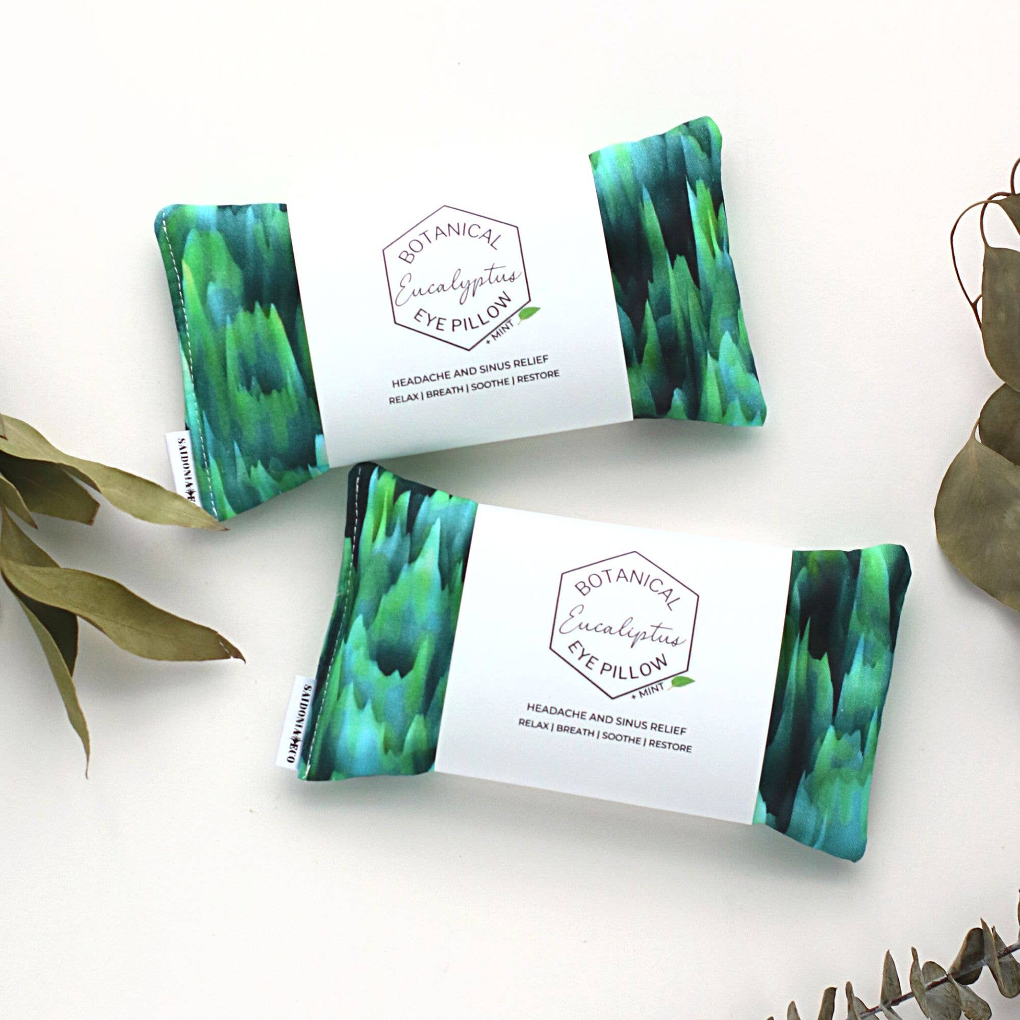 Three Breathe Gift Sets: Winter Eucalyptus Eye Pillows & Handmade Breathe Balms with green and blue tie-dye patterns, displayed on a white background surrounded by eucalyptus leaves from SaidoniaEco.