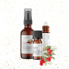 Two bottles of "Joyful Aromatherapy Holiday Blend" skincare products by Wild Nurturer Aromatherapy, with a spray and dropper, decorated with botanical illustrations and a gold confetti background.