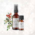 Two bottles of Wild Nurturer Aromatherapy's "Mistletoe & Magic Yuletide Aromatic Blend" with mistletoe and holly decoration on a snowy background.