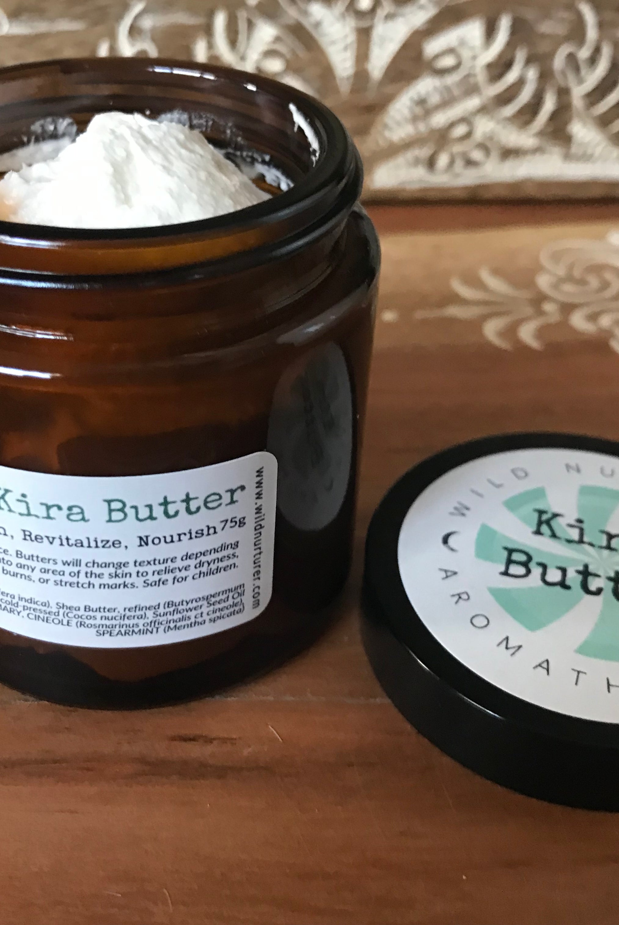 A glass jar of Wild Nurturer Aromatherapy Kira's Collection Rosemary & Mint Body Butter with a white label against a white background. The label includes product details and a green leaf design.